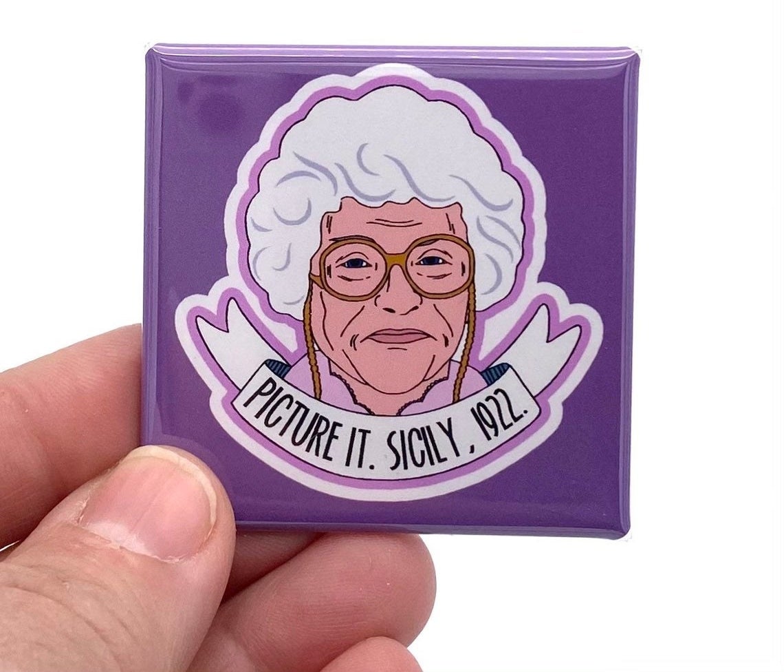 hand holding a square purple magnet with a cartoon of Sophia from the Golden Girls on it with "Picture it, Sicily 1922" on it
