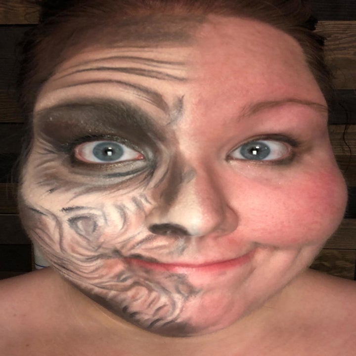 A reviewer selfie showing the left side of their face covered in full elderly costume makeup, and the right side clear of makeup 