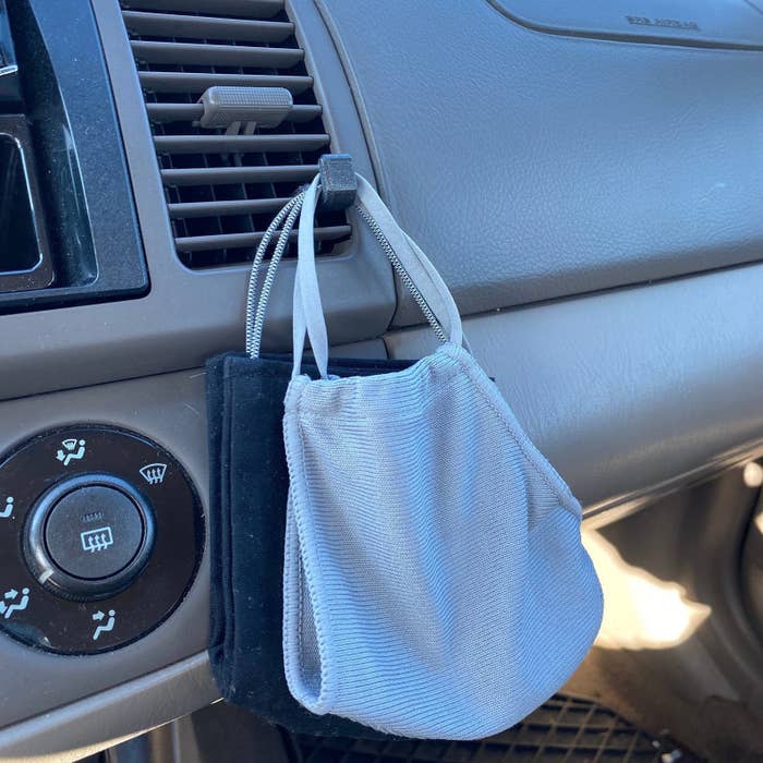 A small gray clip on an air conditioning vent in a car with masks hanging from it 