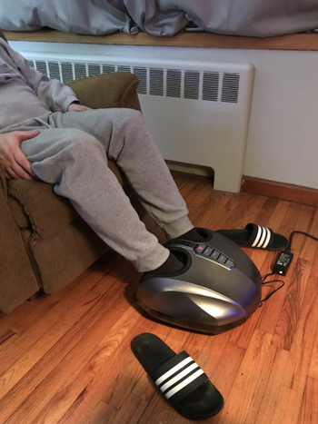 reviewer using oval-shaped silver foot massager with two holes at the top to put your feet in