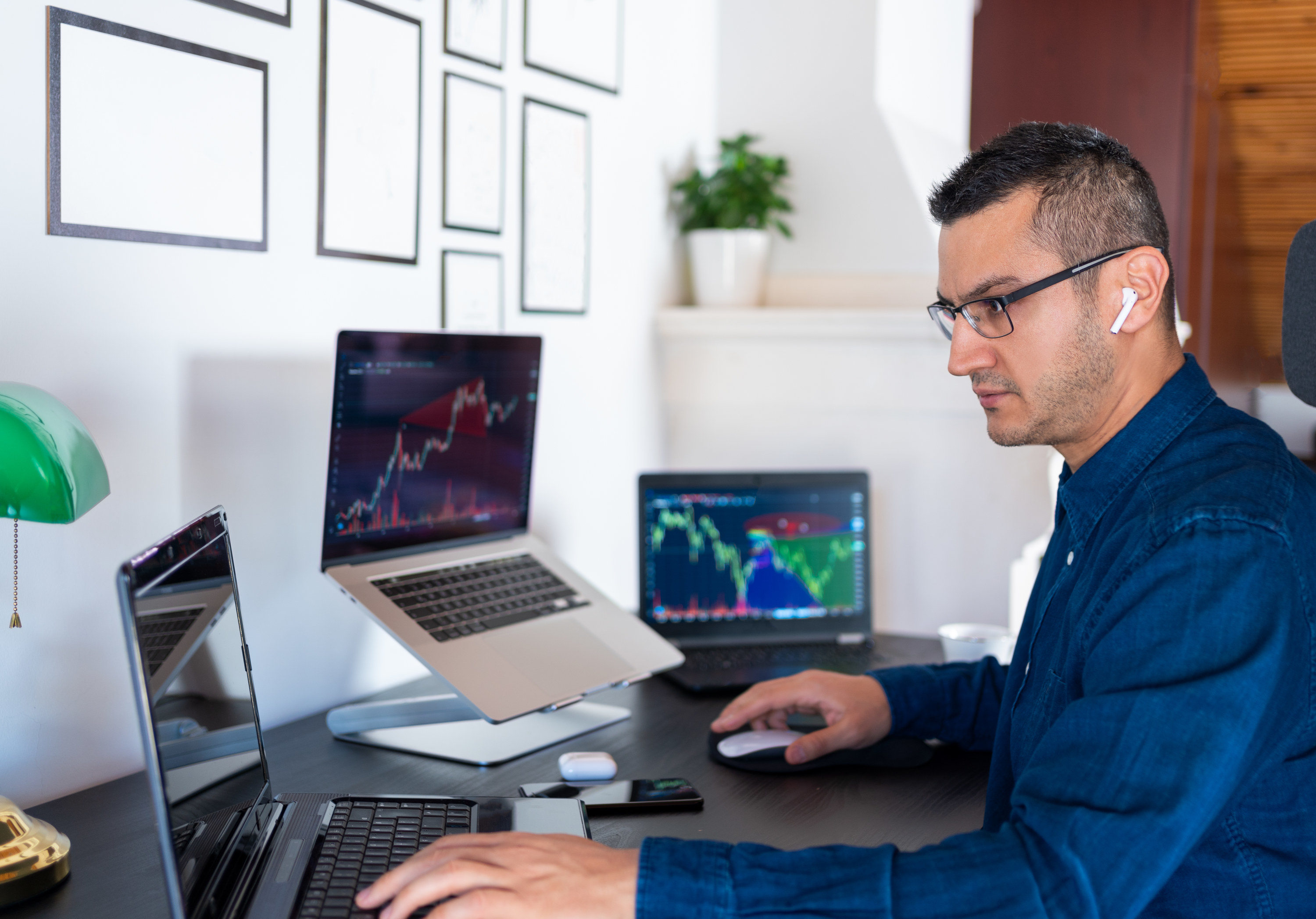 Man looking at his investments on three different laptops in his home office