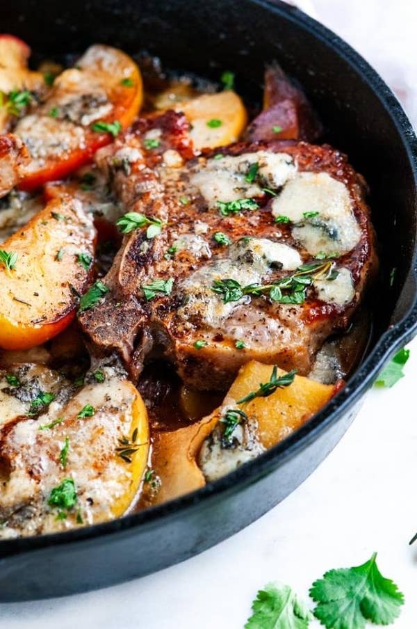A skillet of pork chops with melted blue cheese, pears, and apples.
