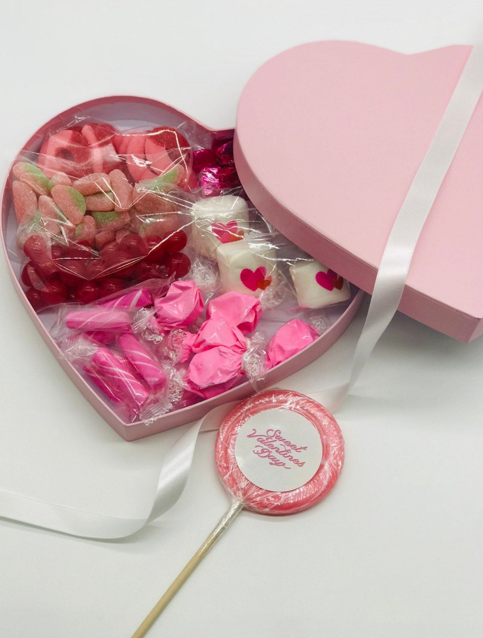 pink heart-shaped box filled with candy and marshmellows in pink and red colors