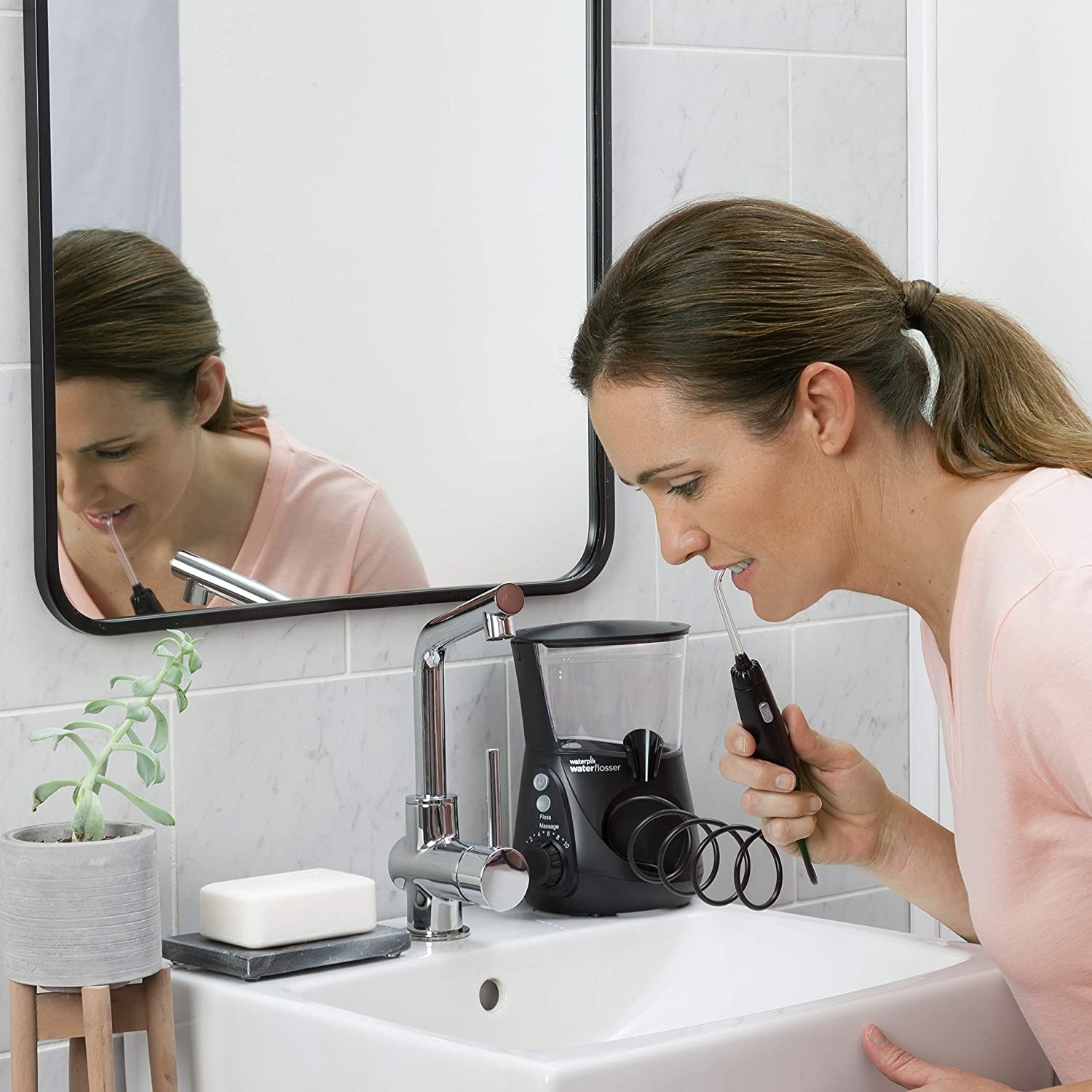 a model uses the black waterpik electric flosser in a bathroom