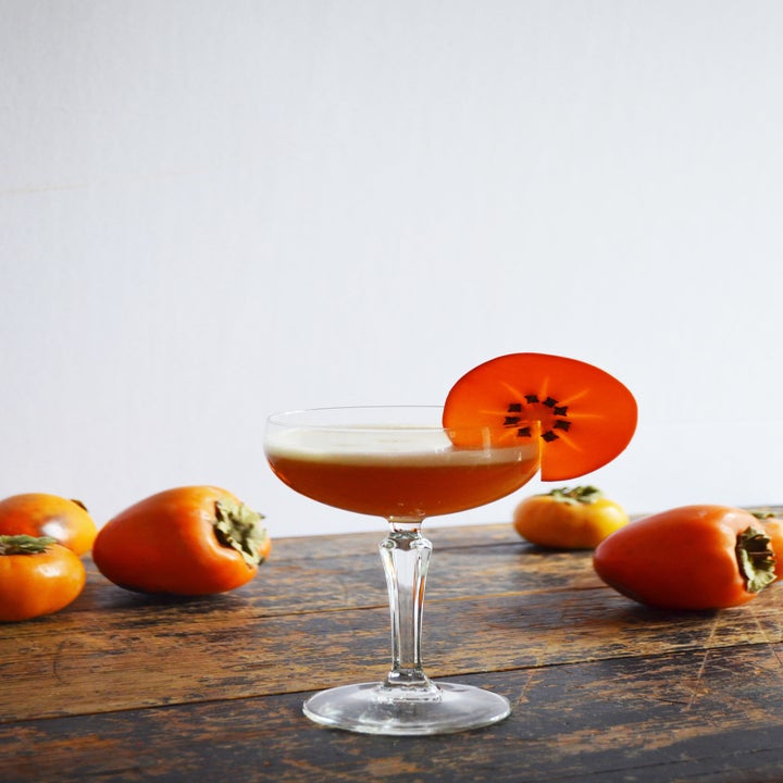 A bourbon amaretto sour in a coupe surrounded by persimmons.