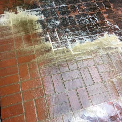 Brick patio with dark black stains washed away on areas where product has been applied with water mixture 