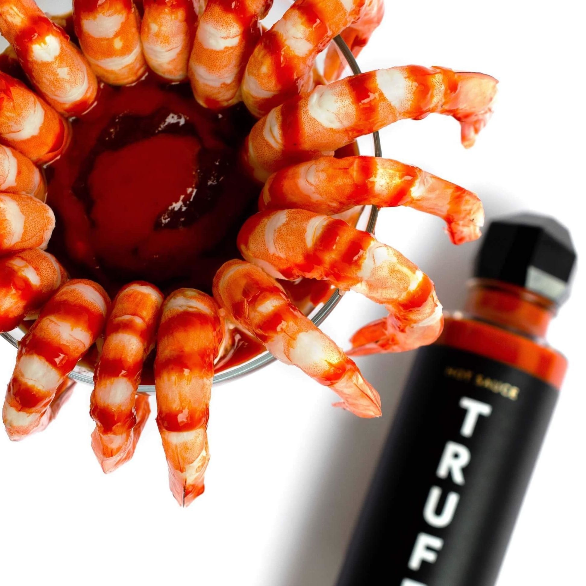 glass bottle of hot sauce with geometric top under glass of shrimp cocktail 
