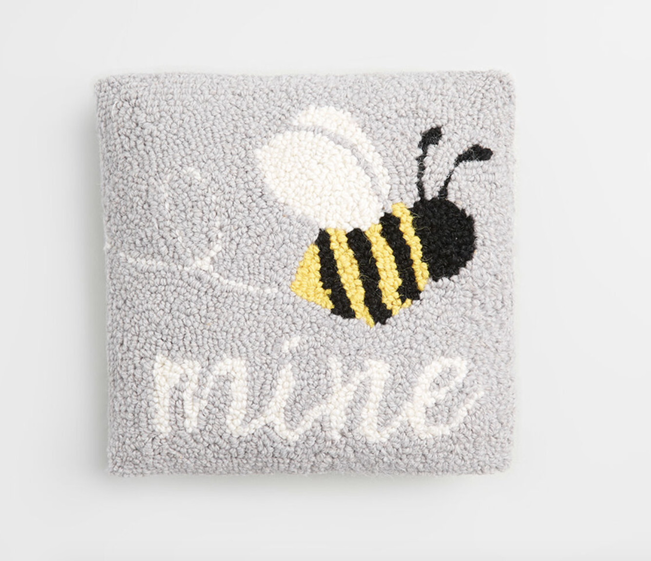 A gray hooked pillow with a bee and the word &quot;mine&quot; woven into it 