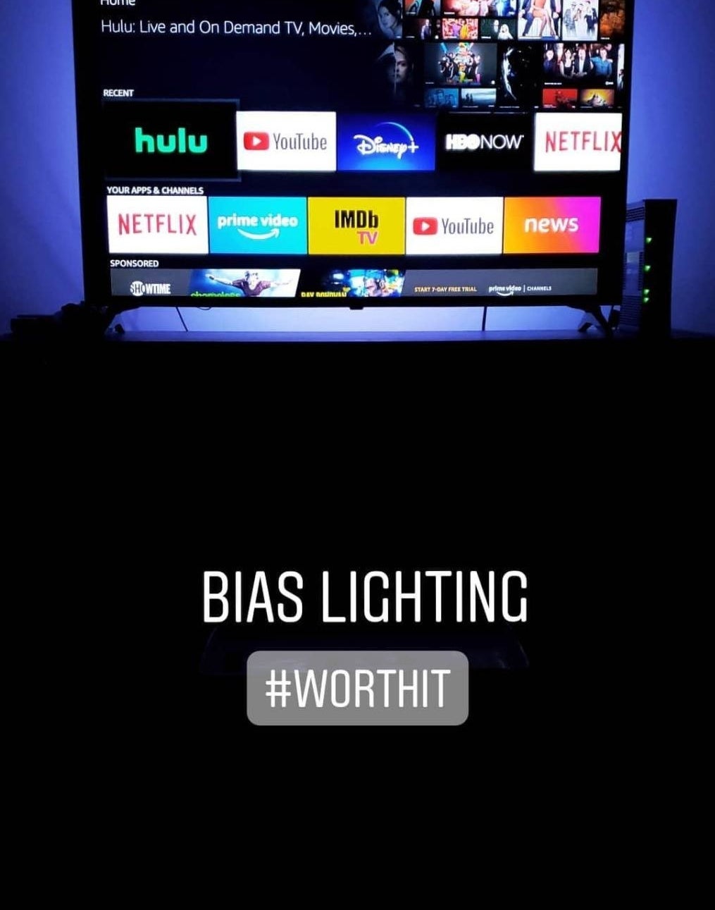 A reviewer&#x27;s photo of their TV with the blue LED lights and the caption &quot;bias lighting #worthit&quot;