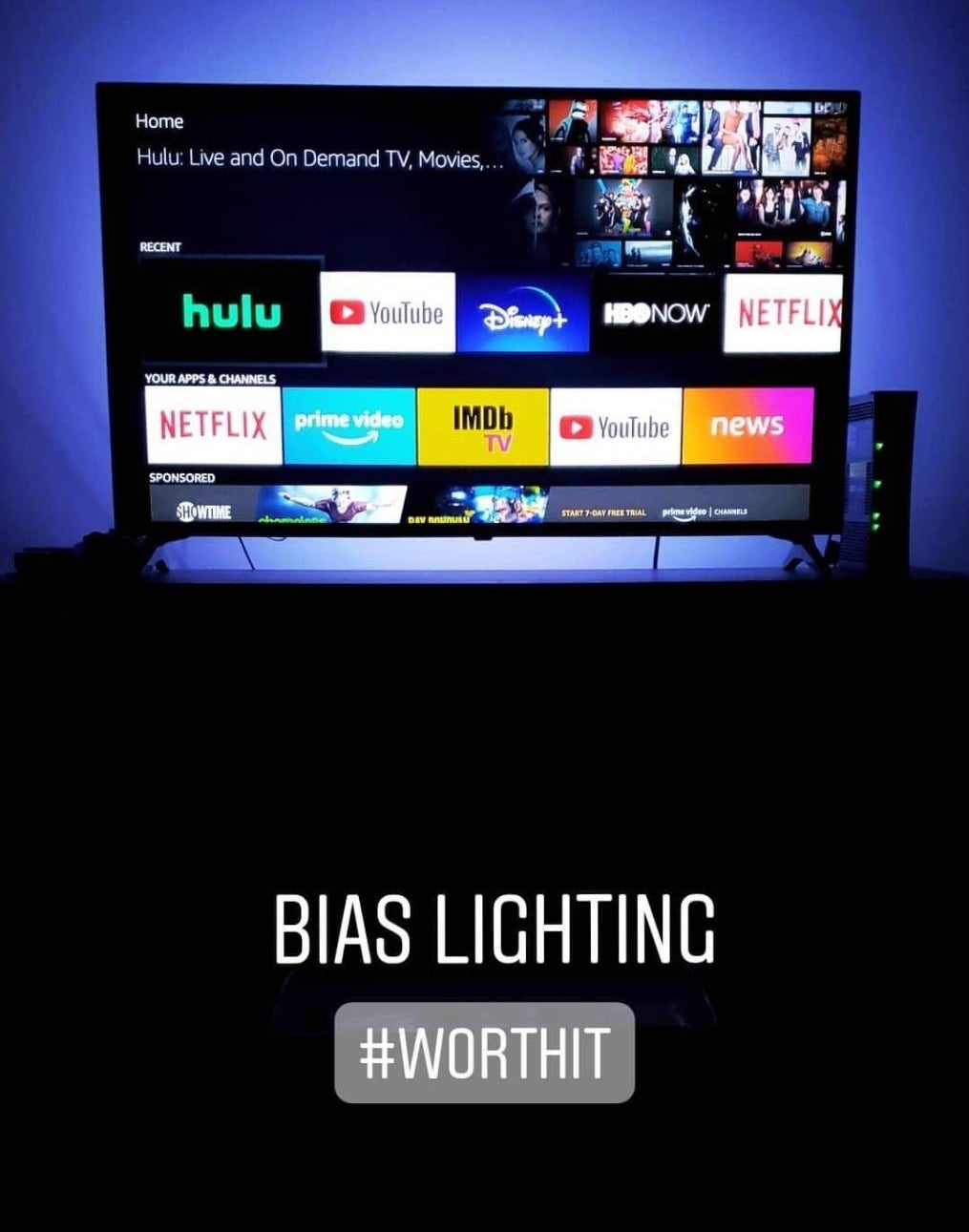 A reviewer&#x27;s photo of their TV with the blue LED lights and the caption &quot;bias lighting #worthit&quot;