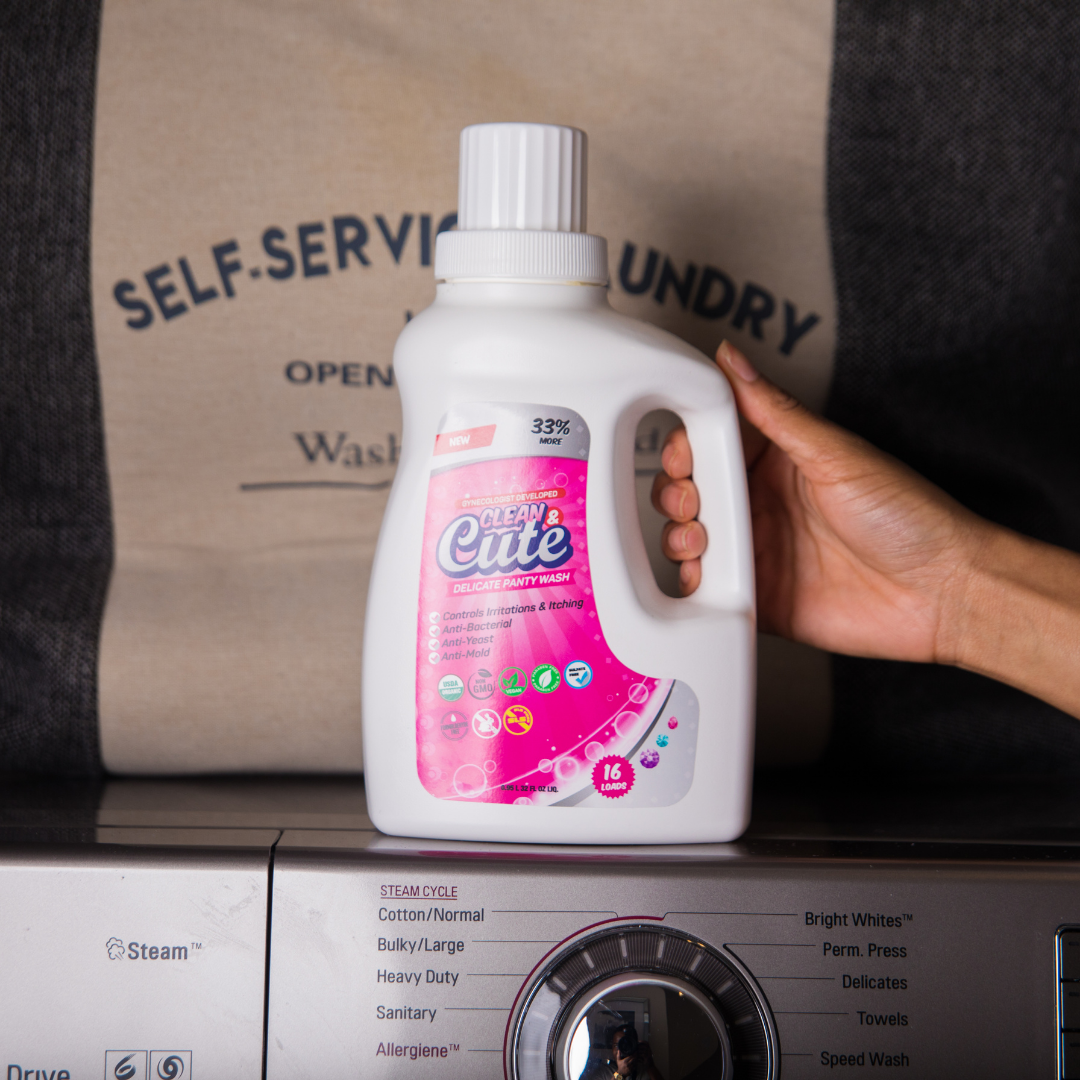 a model&#x27;s hand holds a bottle of Clean &amp;amp; Cute over a washing machine