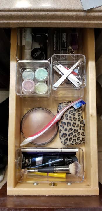 A neatly organized drawer with several clear boxes full of makeup and toiletries
