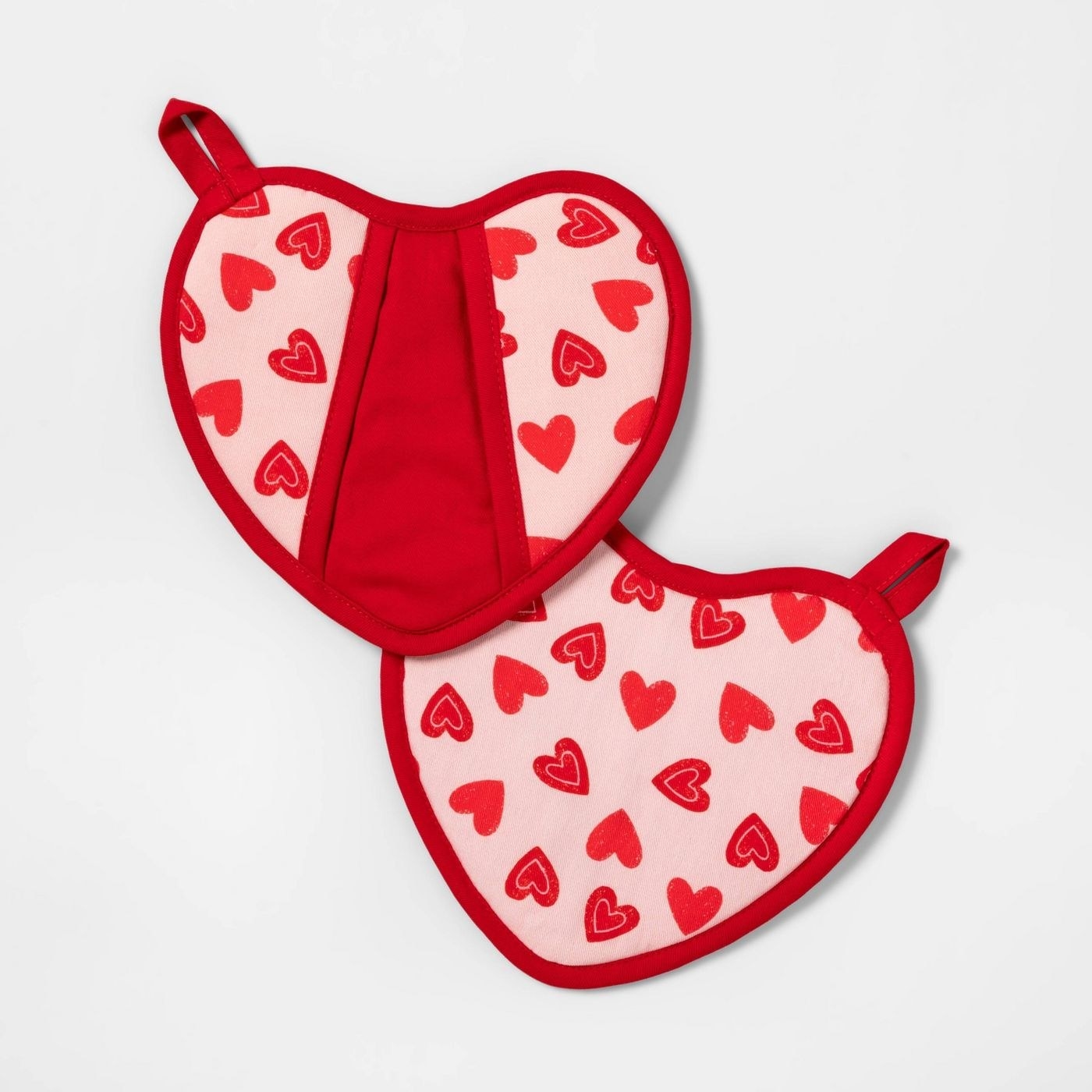 The pot holders, which are heart-shaped, and have red fabric on one side with a shallow pocket for the hand, and pink fabric with red heart prints on the other side