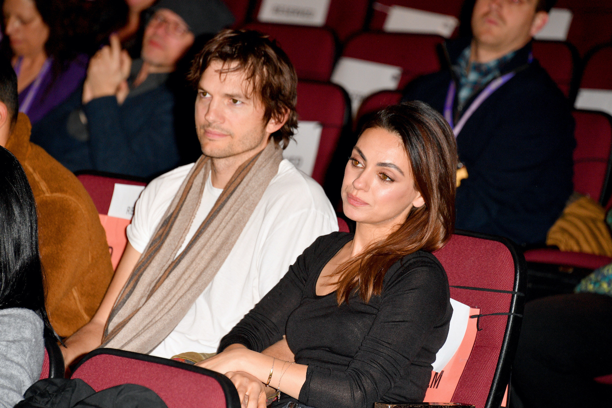 Ashton Kutcher, in a t-shirt and a scarf, and Mila Kunis, in a long-sleeved T-shirt, sitting next to each other during at the 2020 Sundance Film Festival