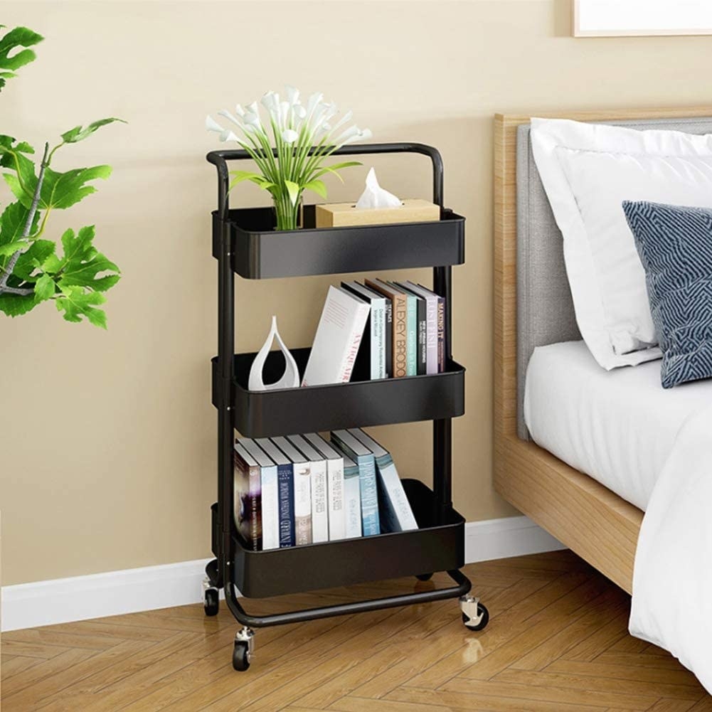 A rolling cart with three deep shelves next to a bed, each basket has a row of books in it