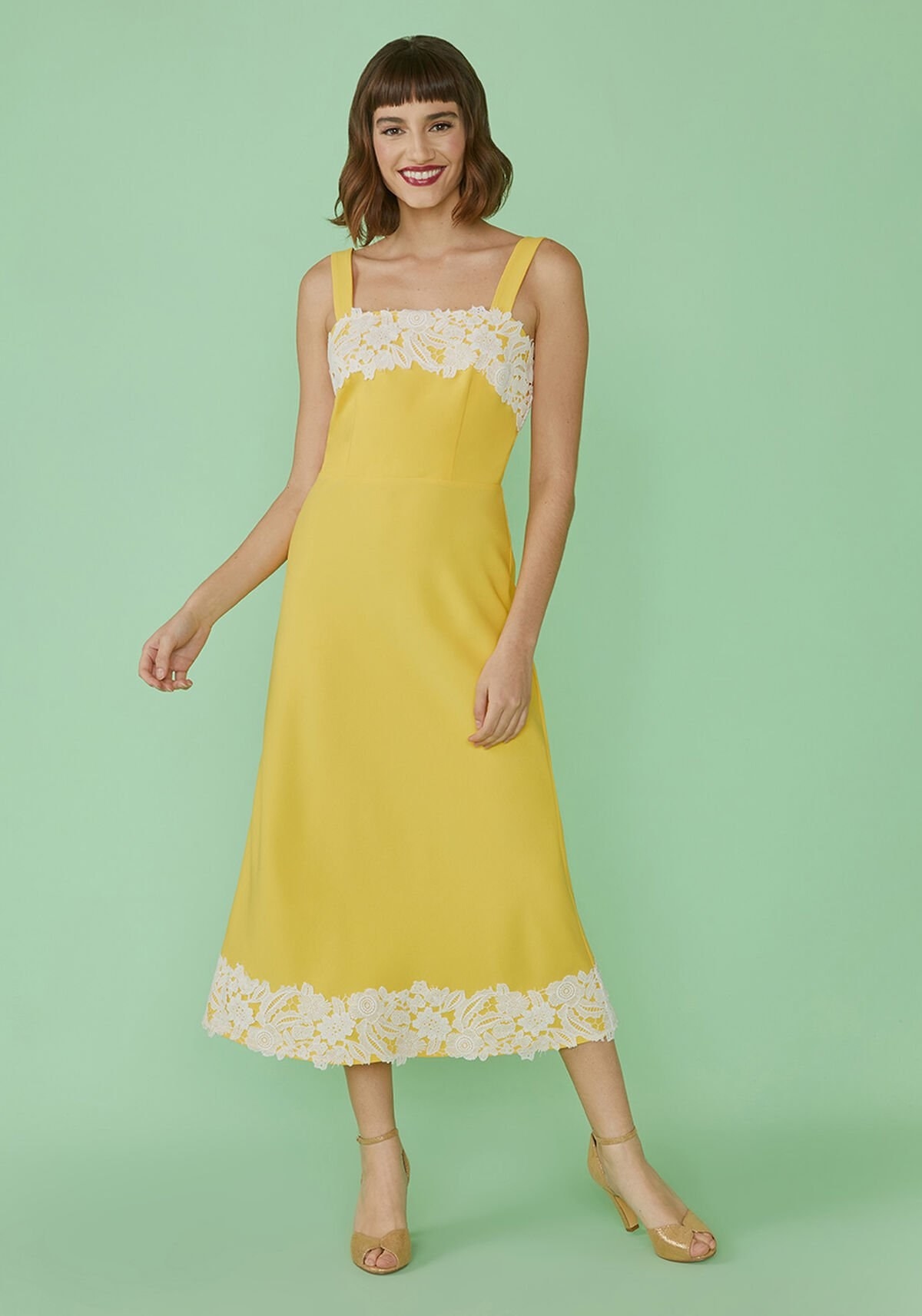 a model wearing a yellow dress with white lace trim along the top and bottom