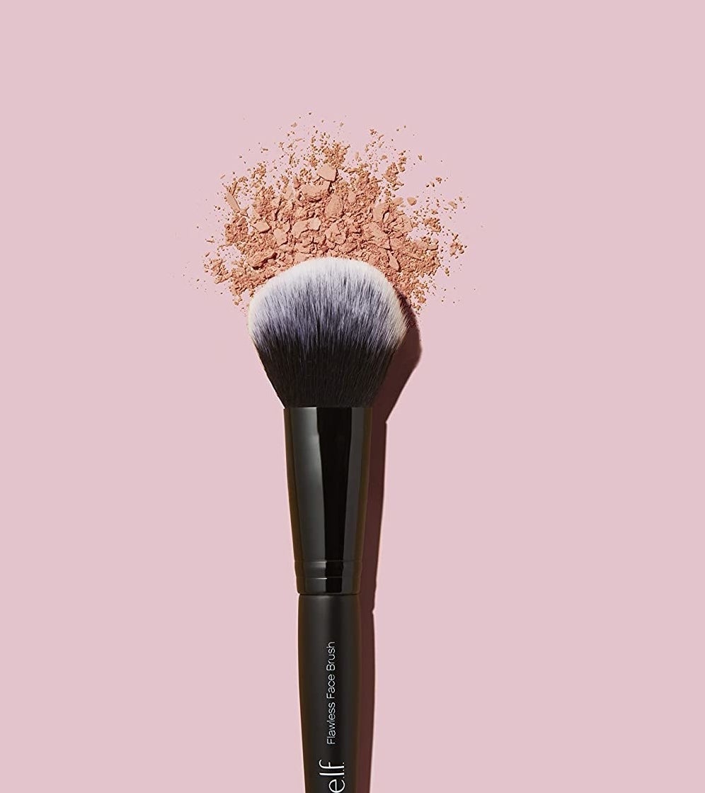 A dense fluffy makeup brush next to a swatch of loose powder