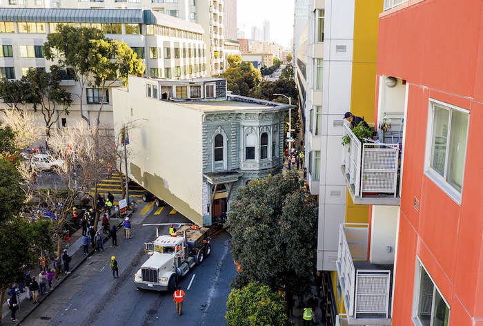 Two-story house is pulled by a truck around a street corner