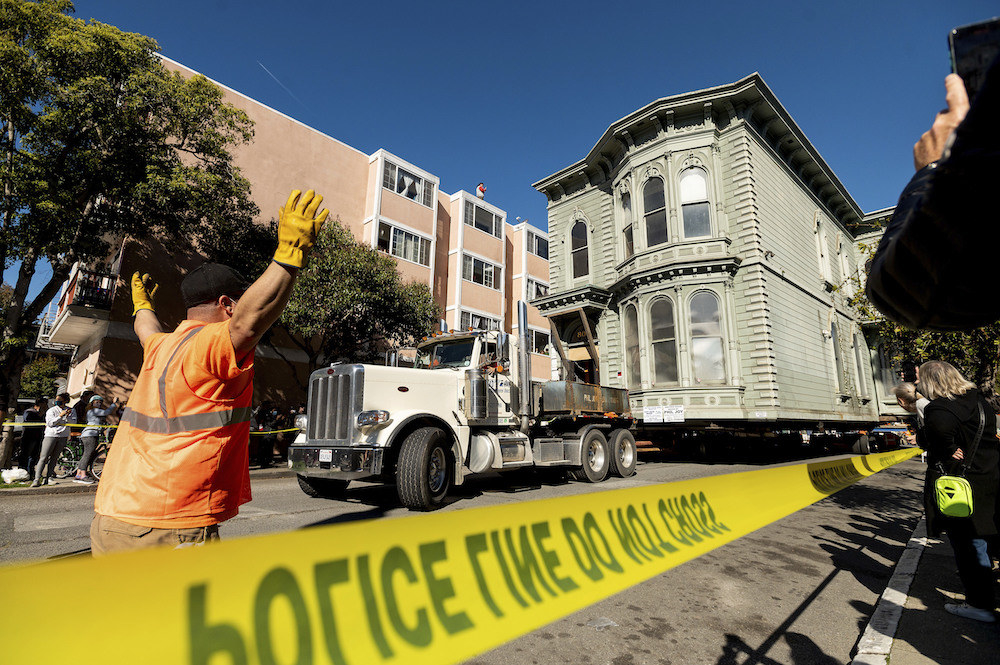 Front view of truck pulling the house along the street, with police line sealing off the area