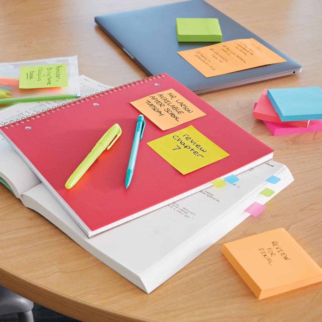 Several packs of Post-It Notes on a desk surrounding notebooks