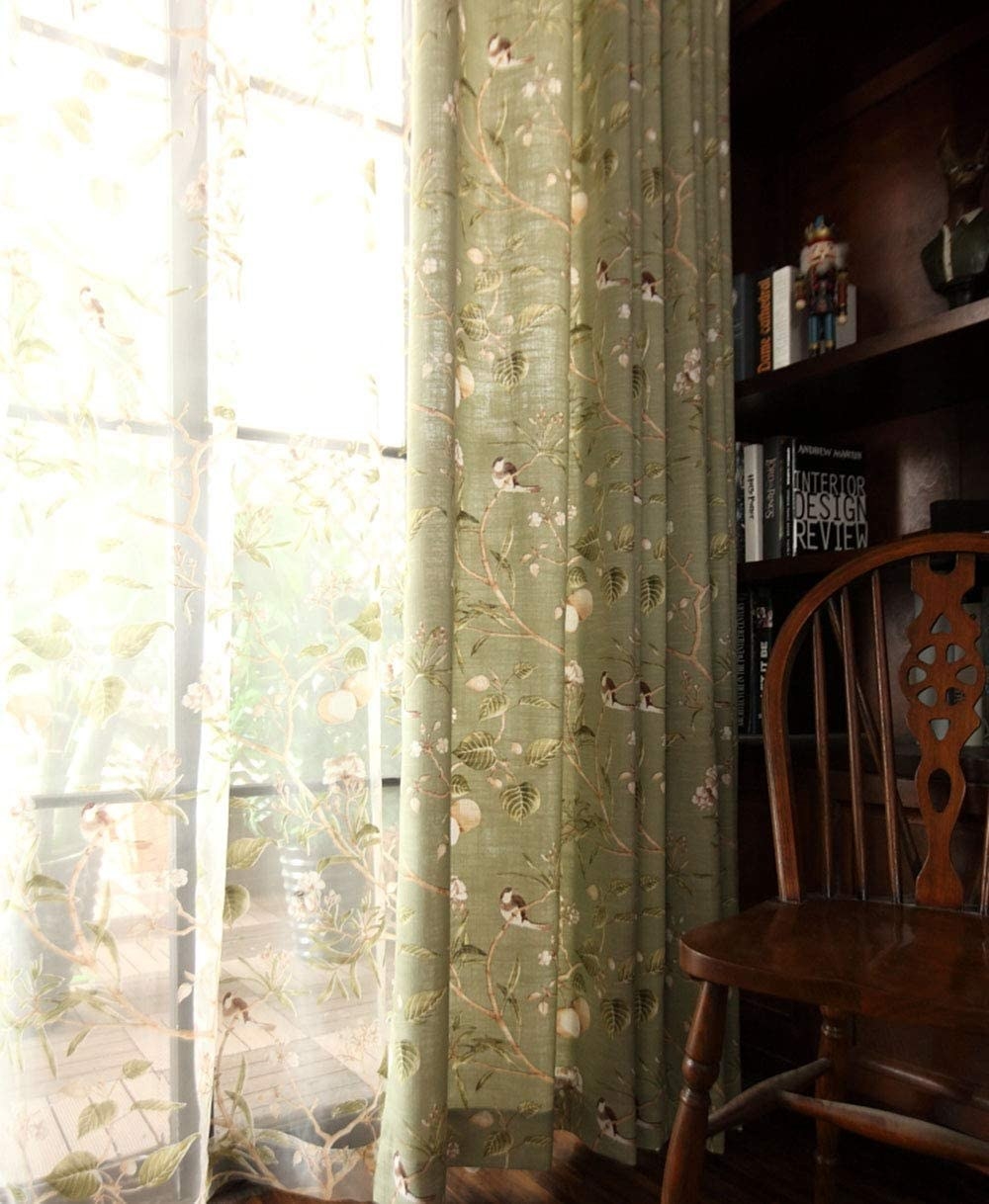 Green curtains with pattern of birds in fruit and leaf covered branches. The inner layer matches the pattern but is on a sheer fabric. 