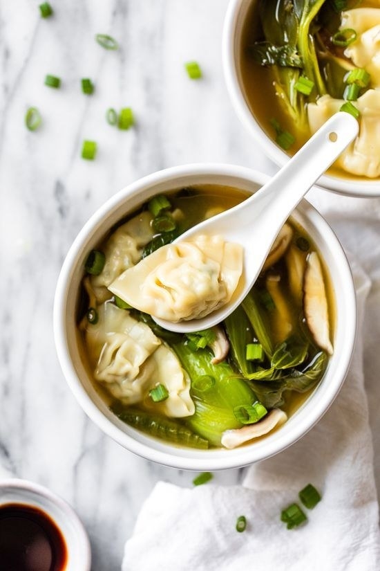 Two bowls of wonton soup with green vegetables.