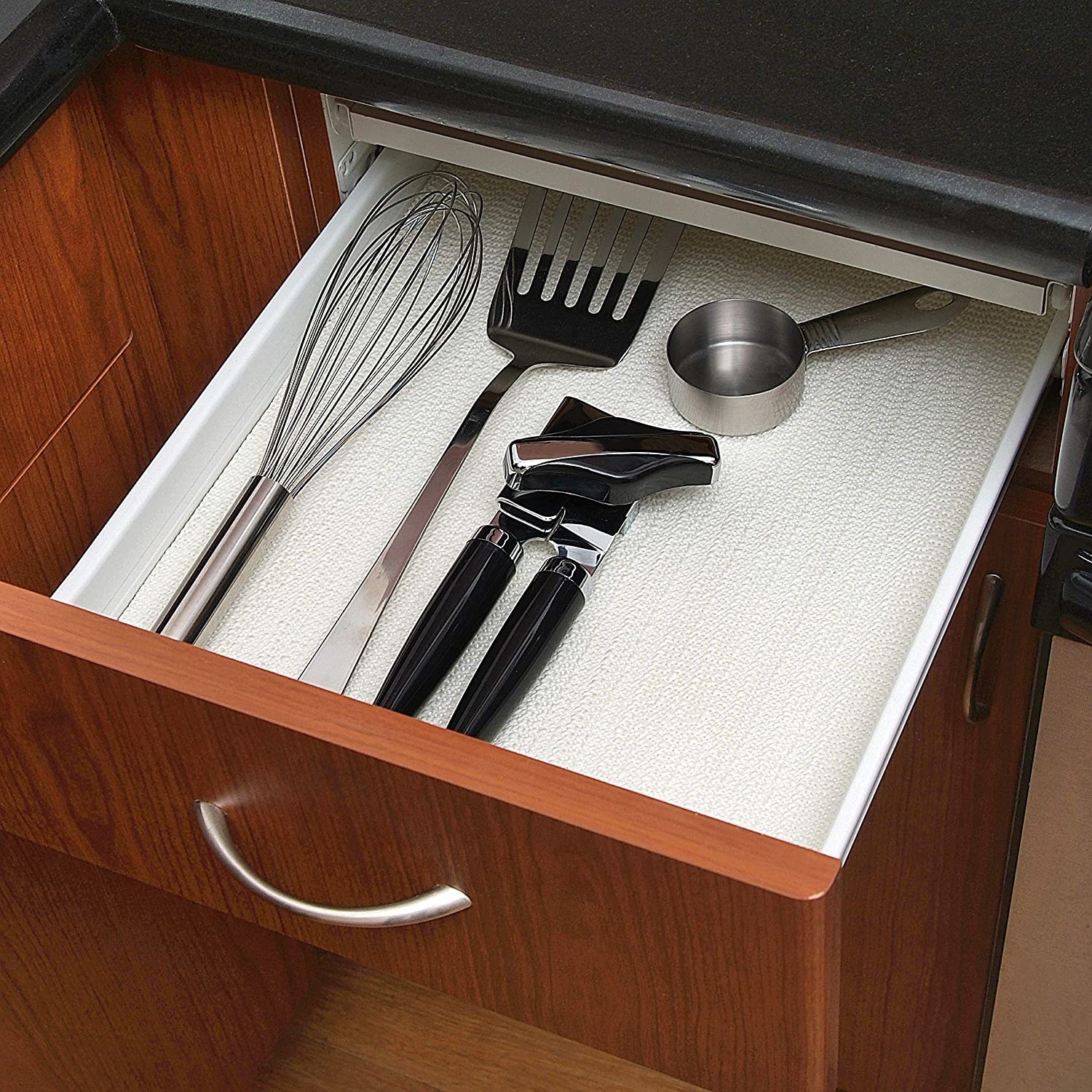Several utensils on top of the drawer liner in a drawer
