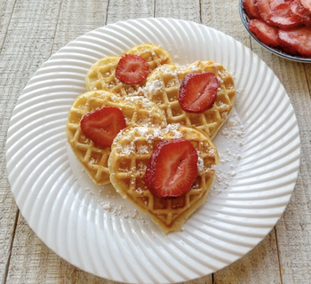 a plate of heart shaped waffles topped with strawberries and powdered sugar
