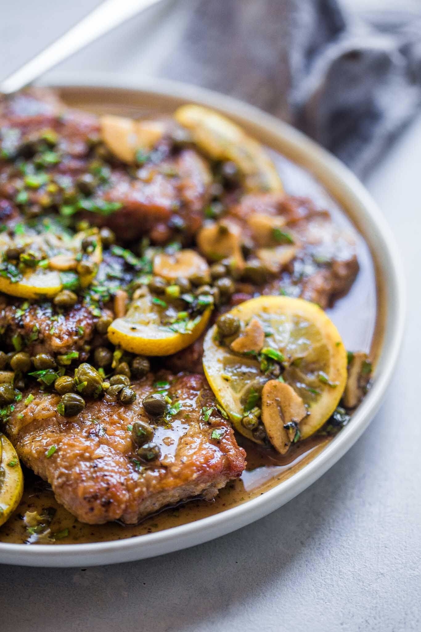 A plate of pork piccata in lemon butter sauce with capers
