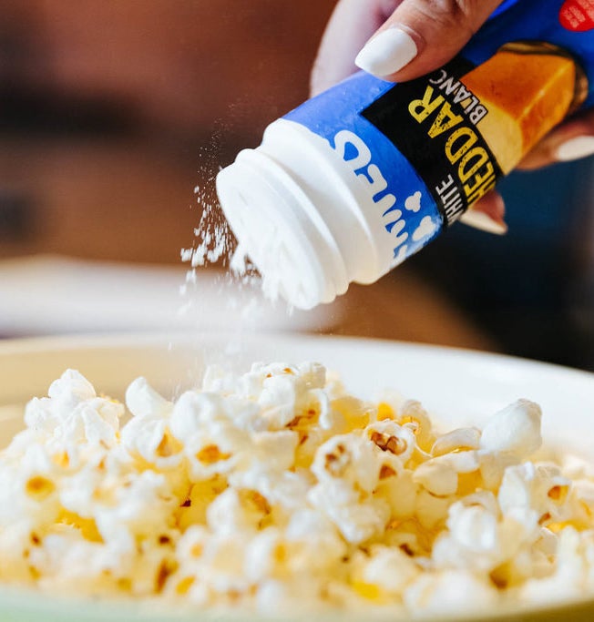 A person shaking the topper onto a bowl of popcorn