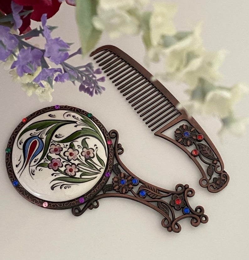 A handheld mirror and comb on a table by some flowers 