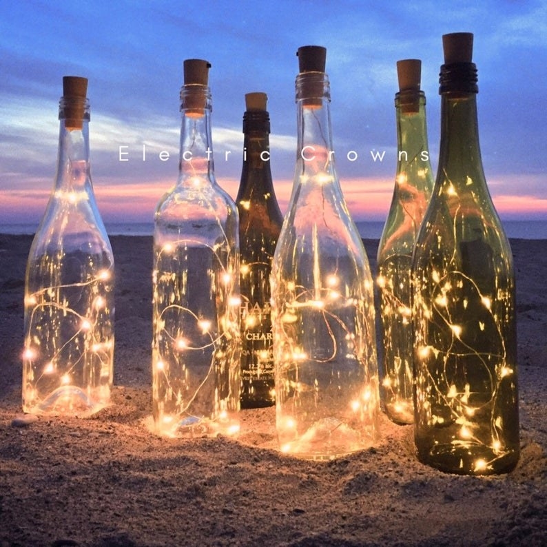 wine bottles with twinkling lights in them on a sandy beach 