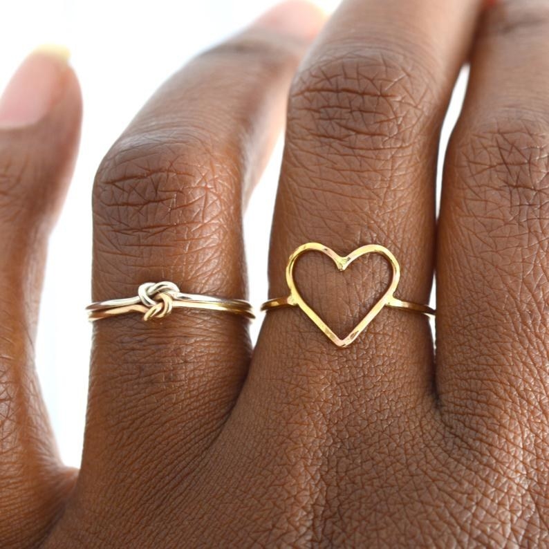 A person wearing a knotted ring next to a heart-shaped ring