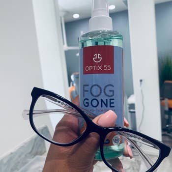 reviewer holding their glasses and a bottle of Fog Gone
