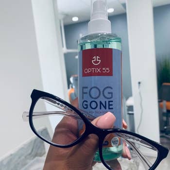 reviewer holding their glasses and a bottle of Fog Gone