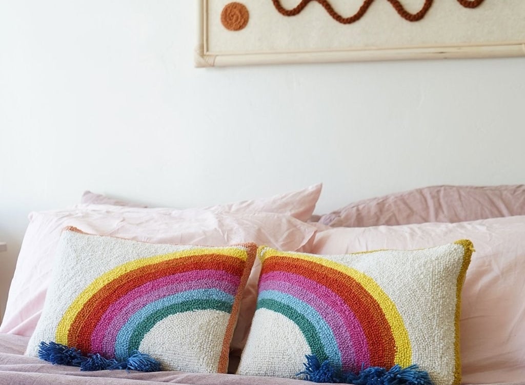 two rectangle-shaped pillows with half of a rainbow on each with blue fringe on the ends of each side of the rainbow
