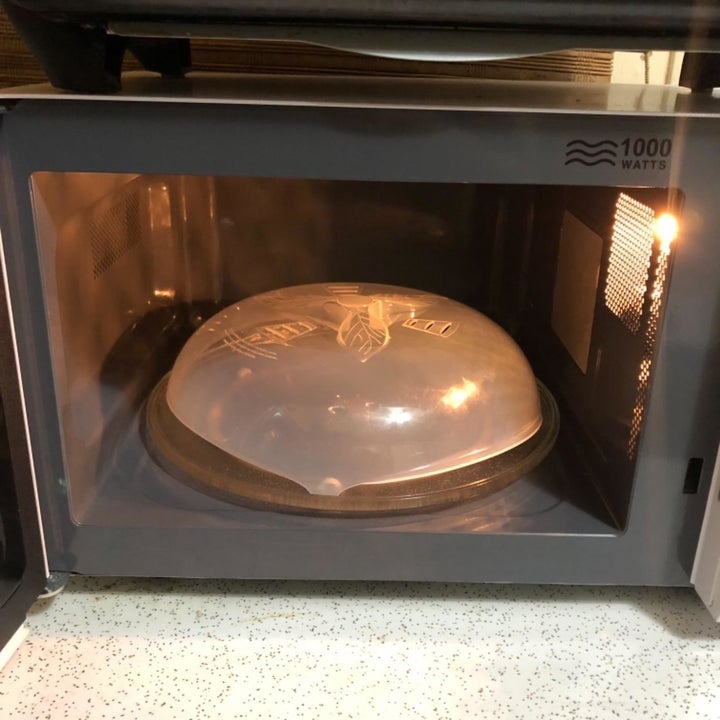 A reviewer photo of an open microwave with the cover over a plate inside 