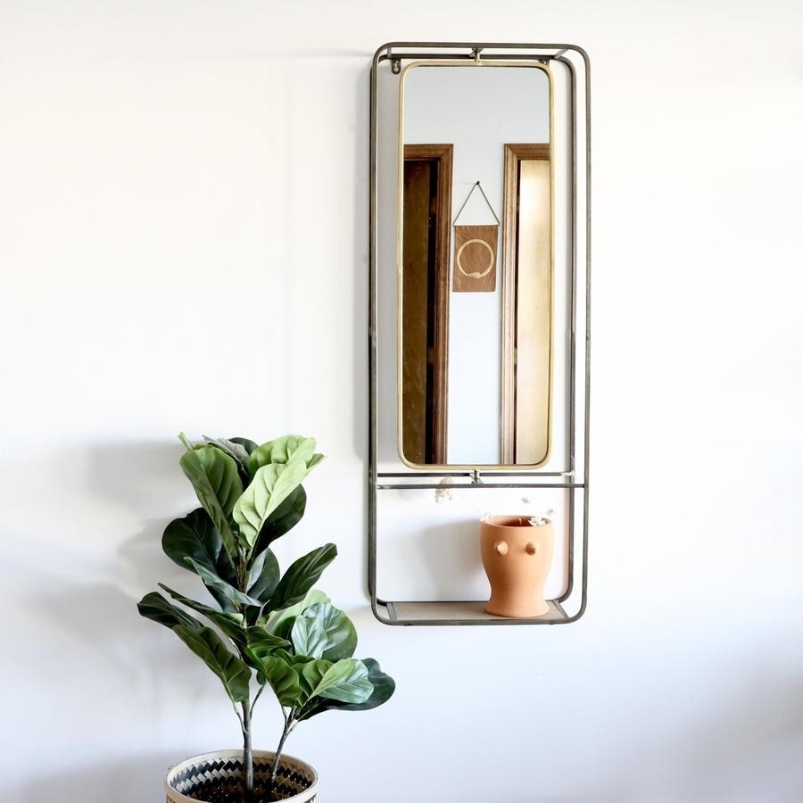 long rectangle-shaped mirror with brass around it and a shelf at the bottom