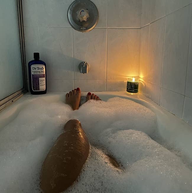 Reviewer in a bubble bath with a bottle of Dr Teal's on display on the edge of the tub