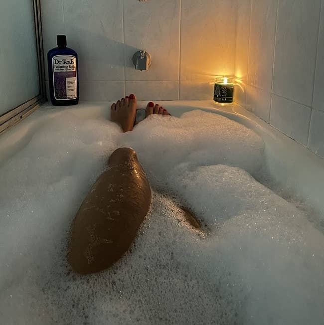 Reviewer in a bubble bath with a bottle of Dr Teal's on display on the edge of the tub