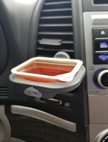 sauce dip clip holding a takeout sauce container while attached to a car's vent