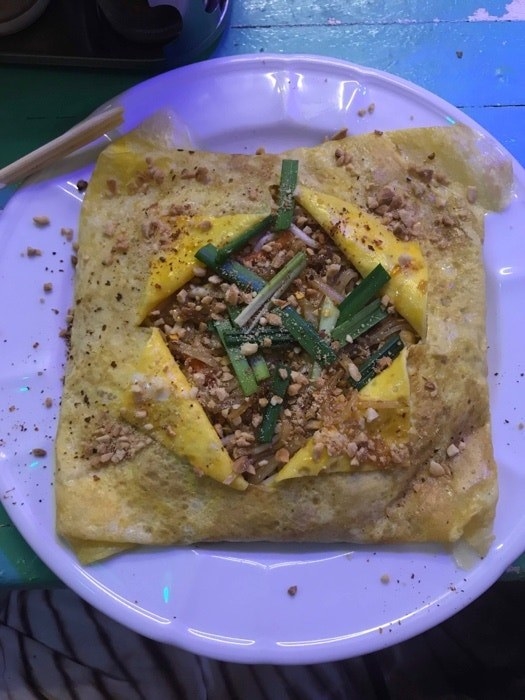 A plate with a square egg crepe cut open in the center to reveal pad Thai noodles topped with peanuts and green onion