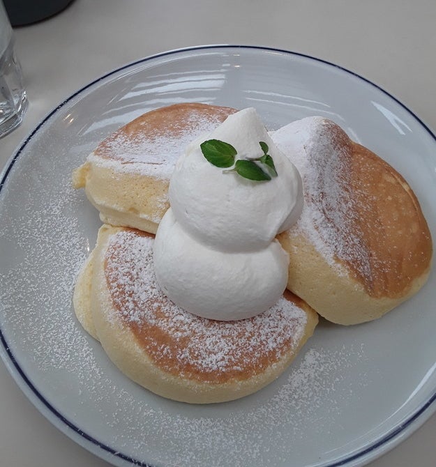 A plate topped with three thick pancakes topped with dollops of whipped cream and powdered sugar