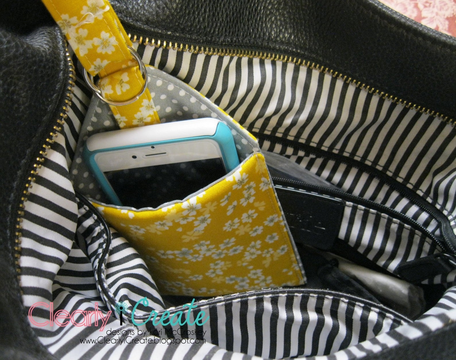 A small yellow floral padded open top phone holder with a phone in it slung on a purse handle 