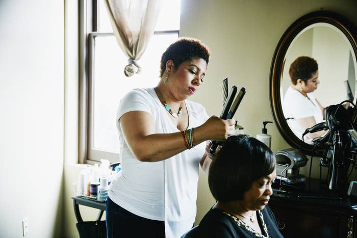 Female salon owner straightening hair of female client in salon