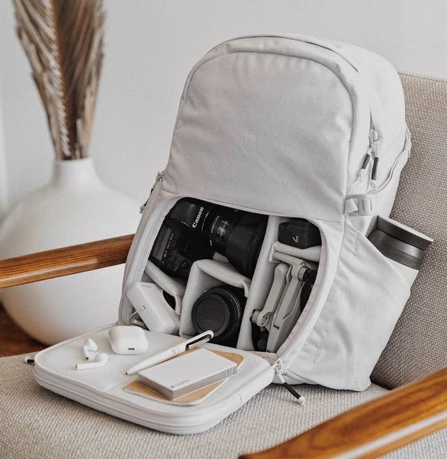 the backpack in white with the front zipper pocket open, showing all the different compartments inside that fit different camera equipment