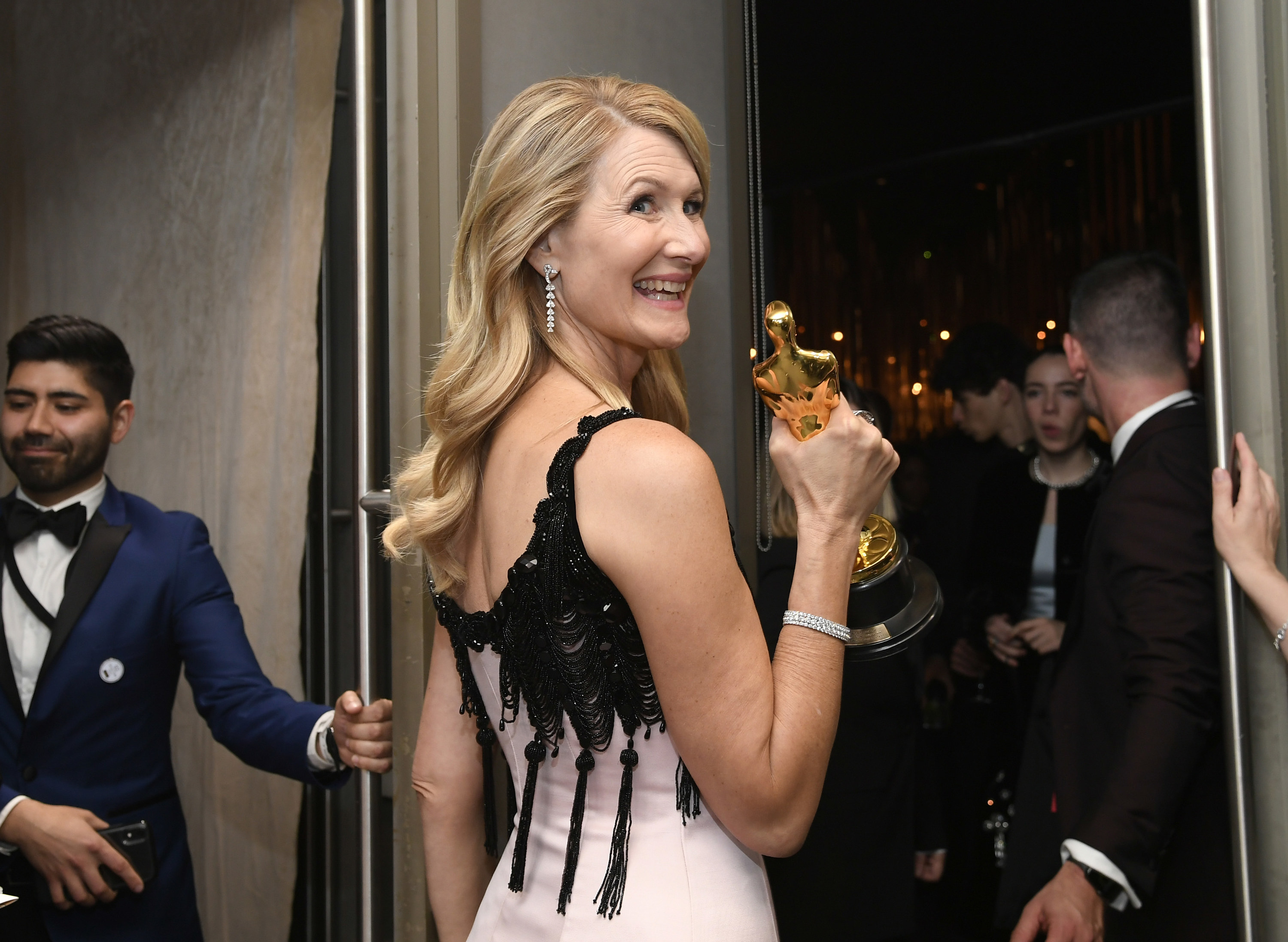 Laura Dern smiling over her shoulder as she holds up her Oscar