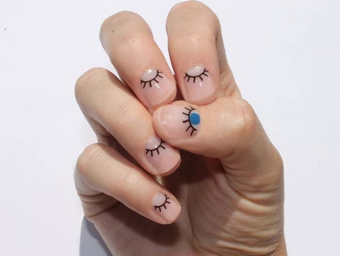 hand with clear, eye-shaped nail wraps on bare nails