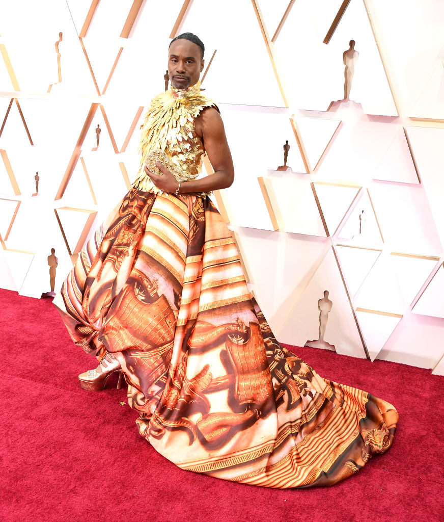 Billy Porter posing on the red carpet in an elaborate print-and-feathered gown and heels