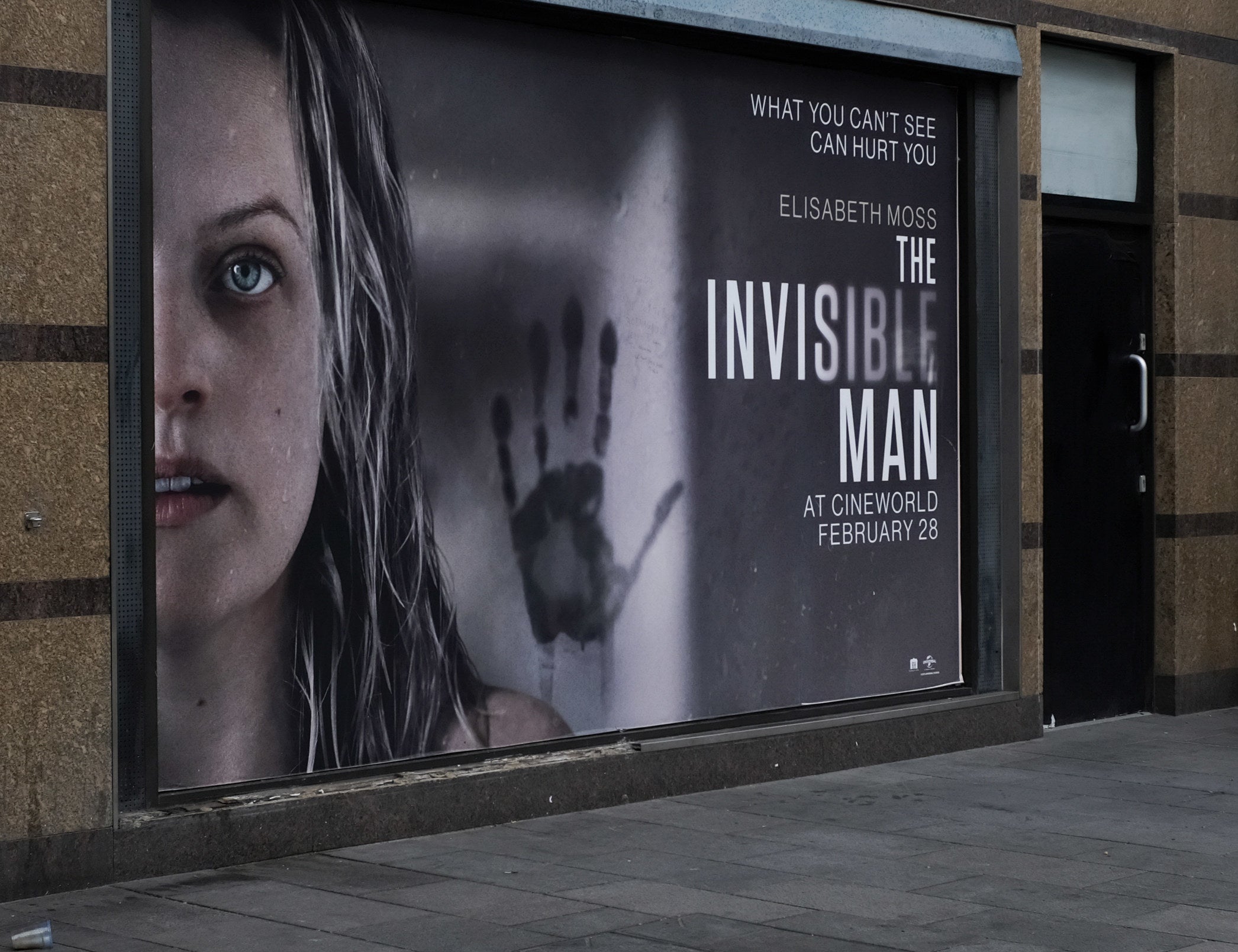 A large poster for "The Invisible Man" on the side of a wall featuring Elisabeth Moss and a handprint